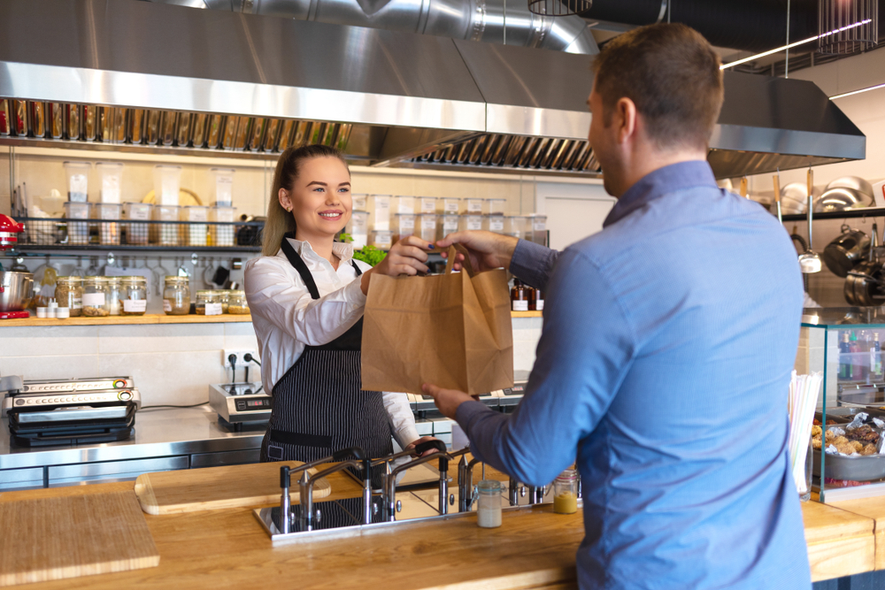 Cheerful,Waitress,Wearing,Apron,Serving,Customer,At,Counter,In,Restaurant